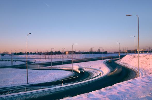 A one quarter of a snowy cloverleaf interchange during the clear blue sky sunset with a pink horizon