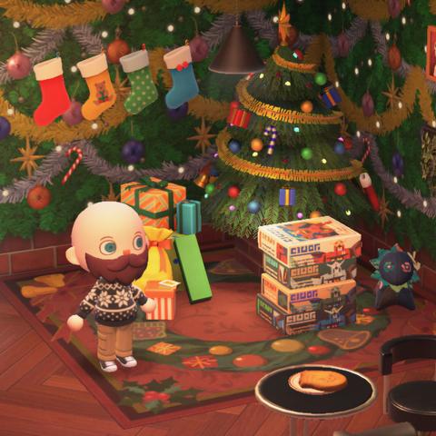 Animal Crossing: New Horizon screenshot. Image shows a bald, bearded light skinned human villager in a black snowflake sweater in a room with herringbone wooden floor and holiday wallpaper. Behind them is a large Christmas tree with wrapped presents, a stack of Gunpla model kits, and a blue plushie. There is a red carpet with a green wreath on it underneath the tree and presents. Four stockings are hung on the wall in a row.