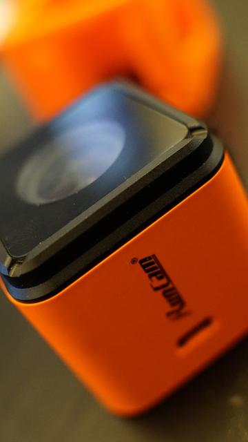Eine RunCam3 in orange
dahinter eine unscharfe TPU-Halterung für die Kamera