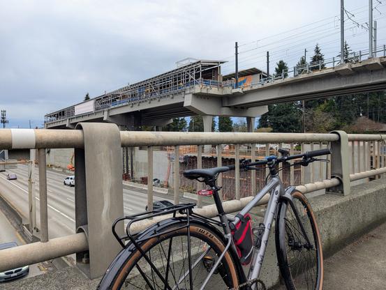 The picture of the NE 130th St light rail station taken from the freeway overpass that runs next to the station. The picture includes my bike on the overpass.