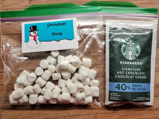 This image shows the interior of a nearby Little Library. In addition to the books on offer there are two sandwich bags, stapled together. One contains a packet of hot chocolate mix powder; the other contains ½ cup of Snowman Poop (mini-marshmallows) ⛄