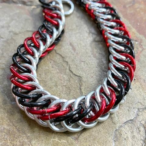 A chainmail bracelet arranged in a loop, consisting of alternating pairs of red and black rings, and in the other 'direction' silver-coloured rings.