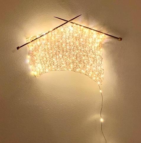 Bijzondere wandlamp. Breiwerk van kerstlampjes aan breipennen die aan een muur zijn bevestigd.