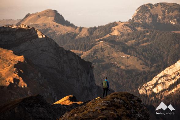 Woman with camera on a rocky outcrop. Mighty mountains in the background.