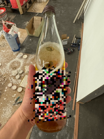Im Vordergrund: Eine Flasche Floramate mit einem Etikett im Design des 38C3. Im Hintergrund: diverse Werkzeuge und Gips