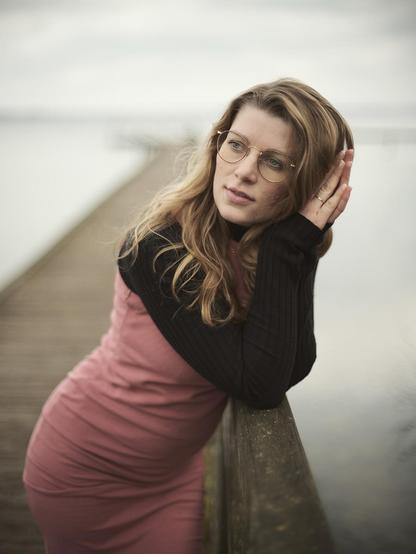 Young woman standing on a jetty, leaning thoughtfully on the railing and looking to the side