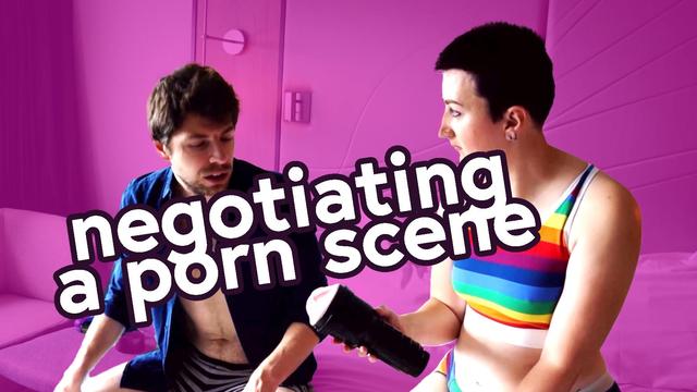 Screengrab of Marcus, a handsome guy with stubble wearing an unbuttoned blue shirt, and Blake, a non-binary person with a short purple crop wearing a rainbow stripe crop top, talking while Blake holds a fleshlight. Image text reads "negotiating a porn scene"