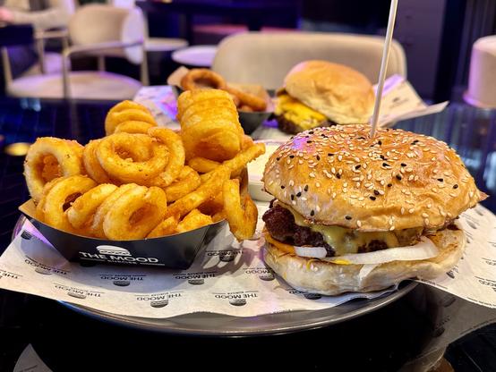 A plate featuring a sesame-seed bun burger with melted cheese, onions, and a battered patty, accompanied by a serving of curly fries in a paper container.