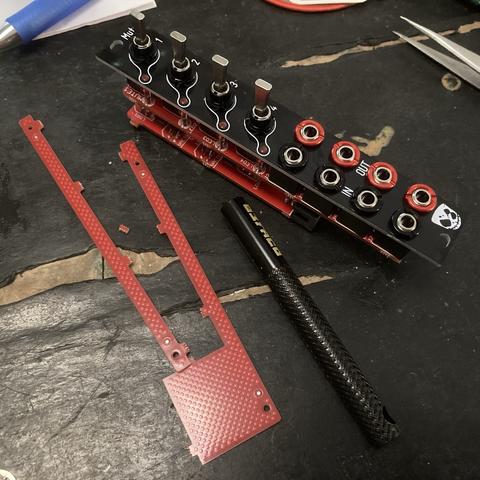 Completed Mutes eurorack module on a tabletop. Jack nut tool and two bits of circuit board snap-off section. Tip of metal tweezers to the top-right corner, ballpoint pen to top-left.