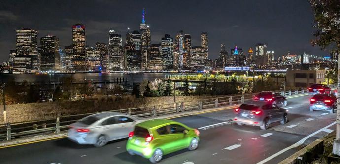 Photograph of the BQE and Manhattan Skyline from Grace Court in Brooklyn Heights. Six cars are in the shot on the BQE in the foreground. In the background we see the full skyline including the Freedom Tower, City Hall, and, off to the right, the Brooklyn Bridge.