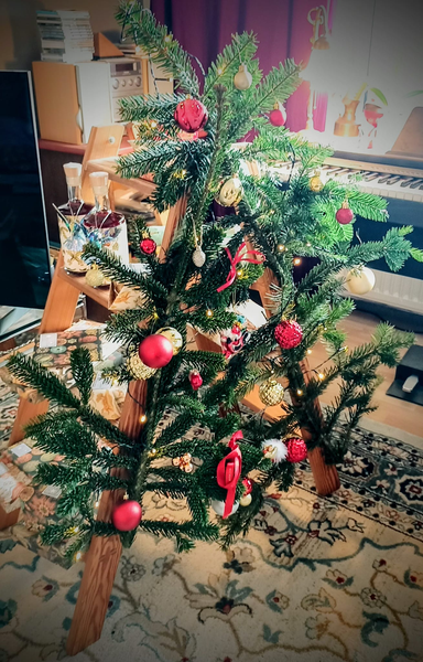 Eine kleine Holzleiter, an der Vorderseite mit tannengrün, Lichterkette, roten und goldenen Baumkugeln.
Auf den Stufen der Holzleiter stehen fertig eingepackte Geschenke...