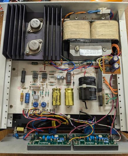 Une alimentation de laboratoire vue de dessus, capot ouvert, au fond une paire de transistors TO-3 montés sur un radiateur, à côté un gros transformateur. Au centre le PCB et sur la face avant 2 voltmètre LCD