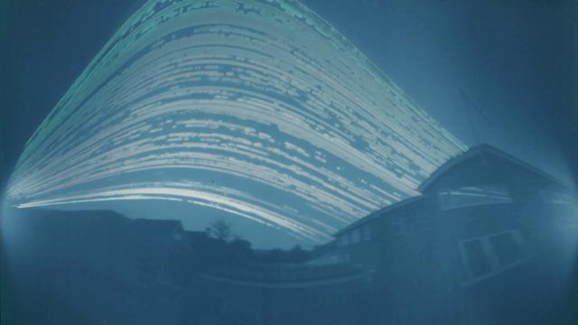Streaks of light curve across the sky. In the foreground is a row of houses on either side.