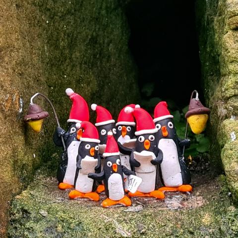A small group of carol-singing penguins all wearing santa hats.