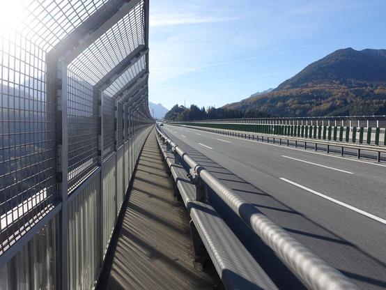 Autobahnbrücke, links neben der Leitplanke ein schmaler Streifen zum Gehen, links daneben ein hoher Zaun am Brückenrand