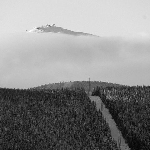 The Sněžka mountain in the distance, rising above clouds. B&W square photo.