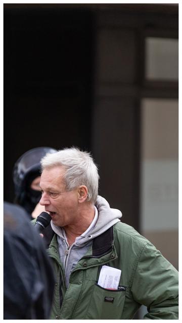 Ein älterer Mann, Christian Worch, mit grauen Haaren und grüner Jacke am Mikrofon