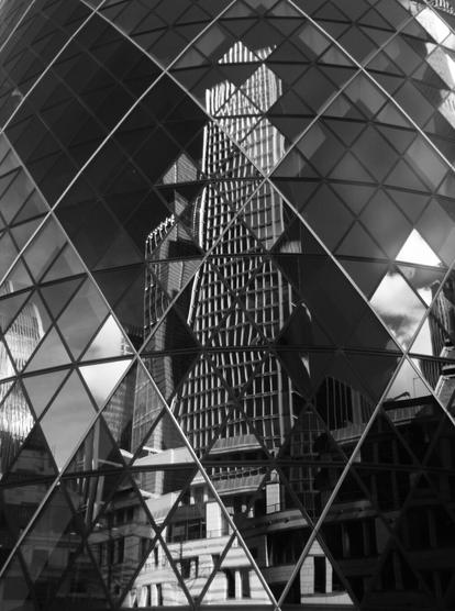 In the characteristic glass façade of the cucumber-shaped building The Gherkin, a neighbouring high-rise is reflected. It's 100 Bishopsgate, which - to my disappointment - doesn't have a proper name. The reflected sky is coloured dark to black because of the infrared. The façade consists of many horizontal rows of alternating glass triangles and diamond shapes. Every four glass panes run thick, light-coloured metal reinforcements diagonally across the outer skin, also forming diamonds. This creates diagonal bands of glass, one of which is darker in colour than the others and stretches from the top left corner of the picture to the bottom right. The fact that each glass pane is slightly curved means that the reflection of the surrounding buildings is not perfect, but creates distortions of the building edges, window struts, roofs, etc., which are symmetrical in reality of course. At the Can of Ham, for example, which protrudes into the picture on the left-hand edge, a whole section appears to have been cut out at the edges of two triangular surfaces, and at 100 Bishopsgate the shape of the roof cannot be recognised. Overall, the photo creates a strong contrast between the chaotic reflections and the very ordered glass façade.