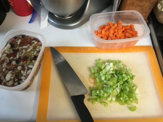 Left: 15 different kinds of beans soaking in water
Center: chopped celery on a cutting board with my chef’s knife.
Upper Right background: chopped carrots in a bowl.
Top edge: my wife’s Kitchen-Aid stand mixer.