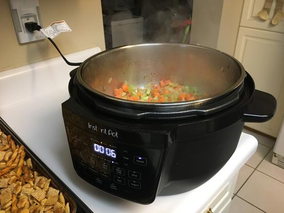 Instant Pot Rio 7.5 quart with the lid off sauteing my vegetables. Steam can be seen rising from the pot. Orange and green vegetables are visible inside the pot.