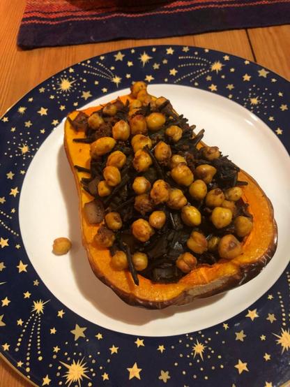 half of a roasted butternut squash filled with wild rice stuffing and topped with crunchy chickpeas siting on a plate edged with stars