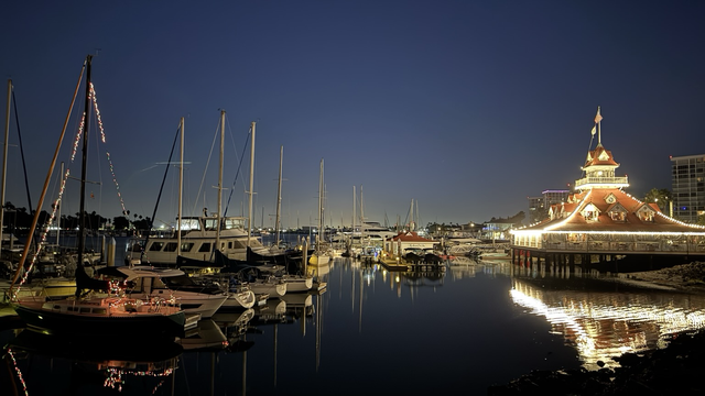 Sailboats in Glorietta Bay Coronado on a moonlit night. The Bluewater Boathouse, with its signature red roof, is festooned with white Christmas lights
