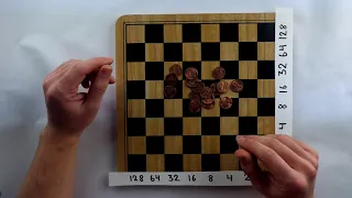 Wooden chess board with binary increasing numbers along two edges, being used with pennies as a calculator.