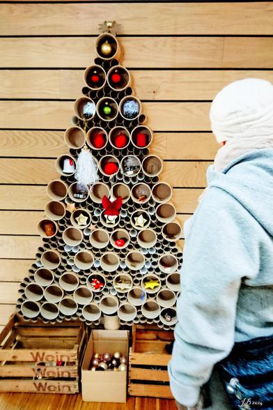 Farbfoto eines "Weihnachtsbaums" an der Wand einer Bibliothek in Tübingen. Er besteht aus Rohrabschnitten mit Weihnachtsdekorationen, die hier geschenkt und entnommen werden können. Sony Xperia Z5 mit Vignette for Android.
