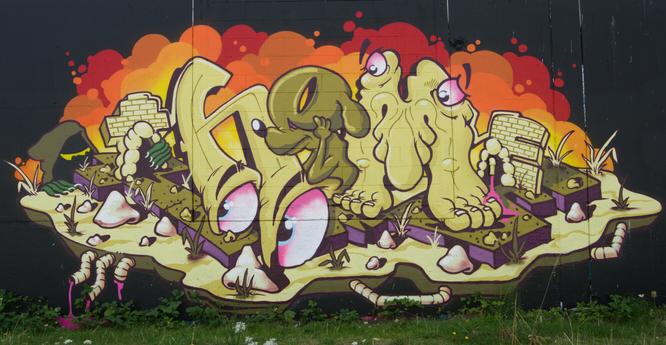 A vibrant graffiti mural depicting cartoonish figures in a whimsical landscape.  Large, stylized feet and a creature resembling a dog with large eyes are prominent.  The background features orange and yellow flames, and the scene includes small, worm-like creatures and small crumbling brick structures. The overall style is cartoonish and playful with bright colors.