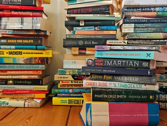 Four towers of used books on a wooden floor.
