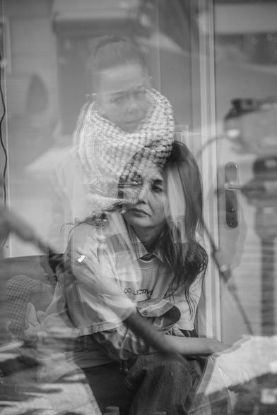 zwart-wit foto van de actrice en activist Carice van Houten. de foto is achter glas genomen, er is een spiegeling van een van de organisatoren in te zien, een vrouw die een Palestijnse keffiyeh draagt