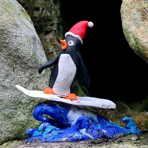 A small model of a penguin surfing while wearing a Santa hat.