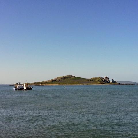 This photo shows the sea, boats and an island in the foreground with a cloudless blue sky in the background.