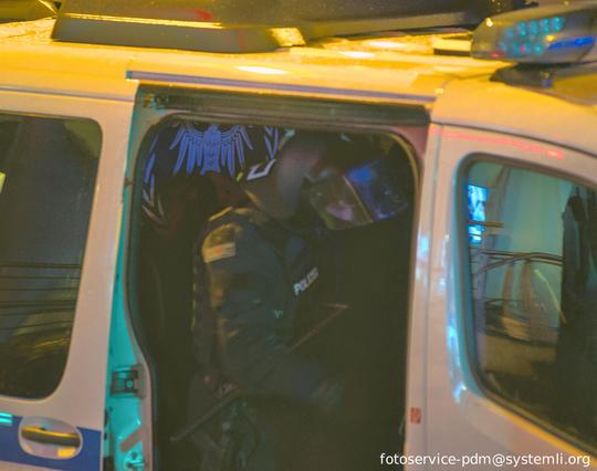 durch die seitentür einer polizeiwanne sieht man hinter einem behlemten cop eine schwarze fahne mit weißem lorbeerkranz und weißen adler der die flügel aufspannt