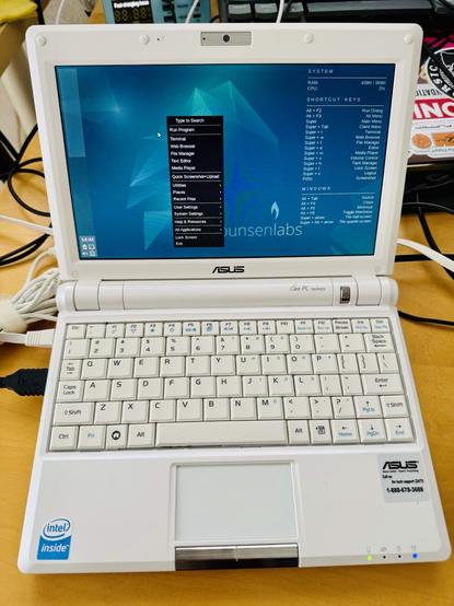 Photo d'un eee PC 900 ouvert, affichant le bureau de BunsenLabs Linux Boron avec un fond d'écran minimaliste et des fenêtres ouvertes.