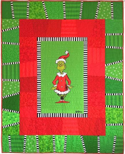 Grinch-themed quilt. The center of the quilt is a panel featuring a standing Grinch in a Santa suit. This panel is surrounded by a series of borders. Innermost is a thin black and white stripe; next a wider scrappy border made up of wonky red blocks. The outside border is also wide wonky blocks, but this time green with thin black and white stripes separating them.