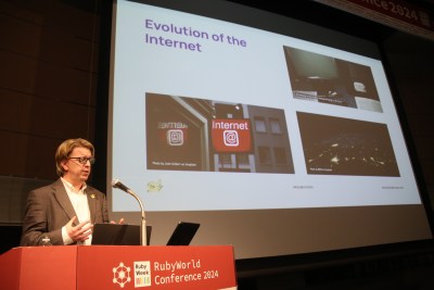 Andy Piper standing at a podium marked RubyWorld Conference 2024, in front of a slide that reads "Evolution of the Internet"