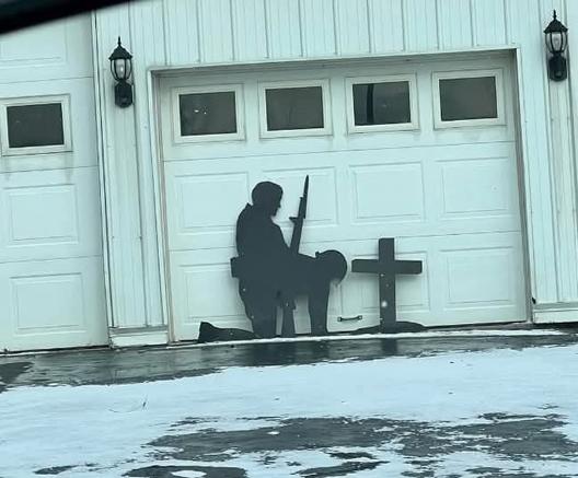 A silhoutte display in front of a garage door. Supposed to be one soldier kneeling next to a cross, his helmet on his knee. However, it looks more like one is bent over and the other is, well, "doing him" doggy style.