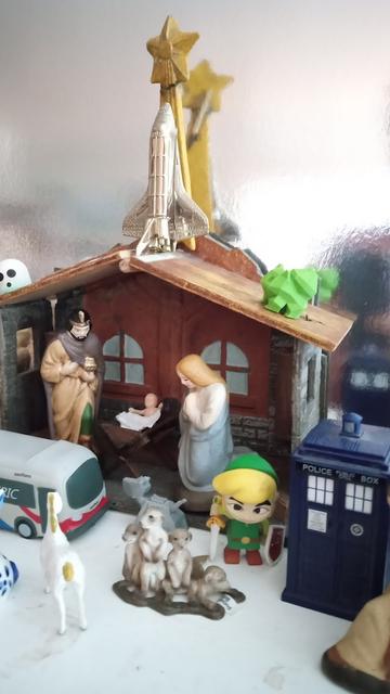 The TARDIS has arrived at Bethlehem. No sign of the Doctor, but K9 is paying his respects to Baby Jesus, as Link stands guard.  The star leading the three wise men appears to be a Space Shuttle.  On the roof there is a Bulbasaur and a Pac-Man-style ghost (the Holy Ghost?). Clean and efficient transportation is provided by a SamTrans electric bus.
