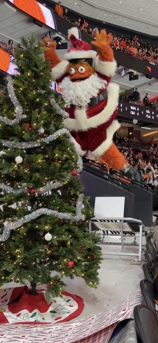 The mascot Gritty dressed as Santa jumping on a Christmas tree