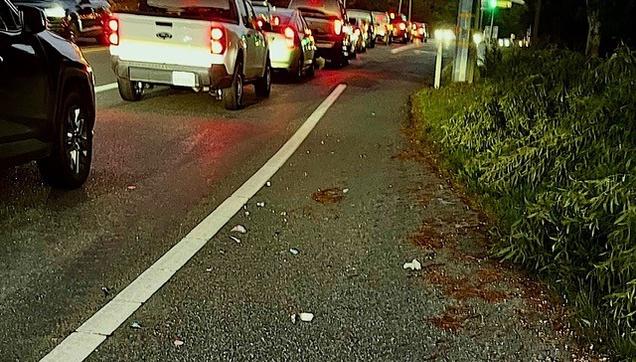 Broken parts of a motor vehicle are littering a long stretch of bicycle lane. The motor vehicle travel lanes are filled with heavy traffic.