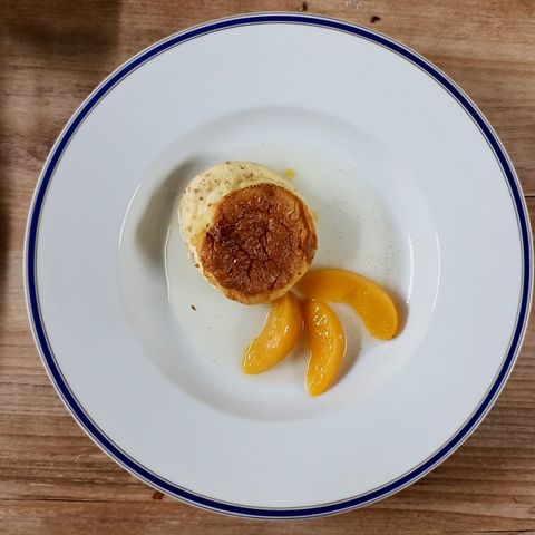 ein kleines Soufflé auf dem Teller mit 3 Pfirsichspalten und etwas Sirup