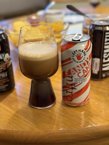 A stout glass of nitro beer sheeting its bubbles in a creamy tan. The pint can is wrapped in white, red, and silver diagonal stripes