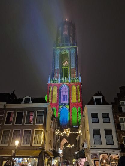 Photo of a cathedral, very tall. With bright red, green and yellow projected on to it. Windows are bright green and yellow, with the building bright red.