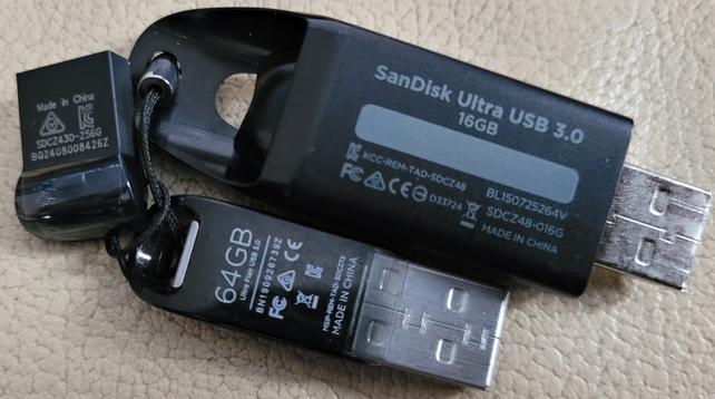 3 SanDisk memory sticks, connected by a cord. The biggest one is 16 GB. The medium-sized one is 64 GB. The tiny one is 256 GB.