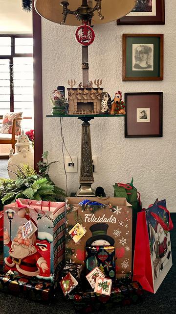 A bunch of Christmas presents at the foot of a tall lamp