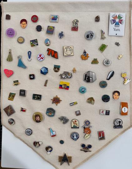 Dozens of pins arranged haphazardly on an off white cloth banner.