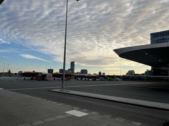 A photograph taken at the Den Haag Centraal Bus Stop, featuring the sky with numerous white clouds