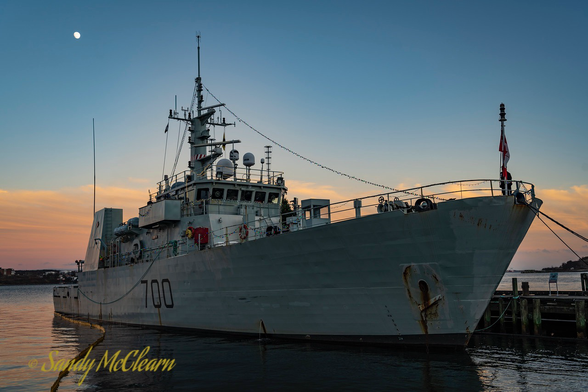 Small warship along a wharf at dusk with a full moon high in the sky.