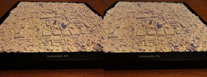 Closeup of a white, 3D printed relief of Lancaster City, Pennsylvania in a black frame, with the legend “Lancaster, PA” printed in silver lettering on the frame. Presented as a Parallel Viewing stereoscopic image.